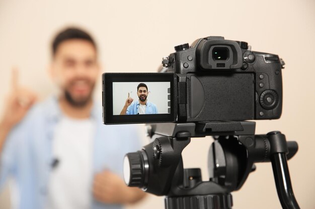 Jeune blogueur filmant une vidéo avec une caméra sur fond beige se concentrant sur l'écran