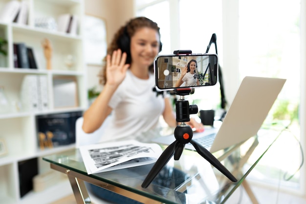 Jeune blogueuse bouclée enregistrant une vidéo à table à la maison