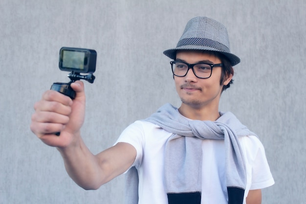 Une jeune blogueuse avec un chapeau et des lunettes tire une vidéo de vlog sur une caméra d’action.