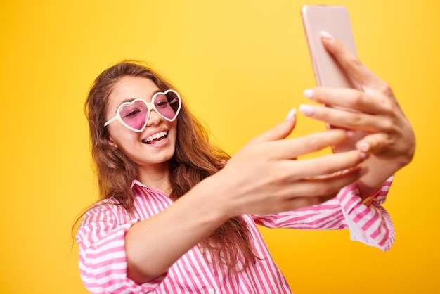 Jeune blogueuse drôle Asian girlmakes selfie sur l'appareil photo du téléphone sur fond jaune, isolé en studio