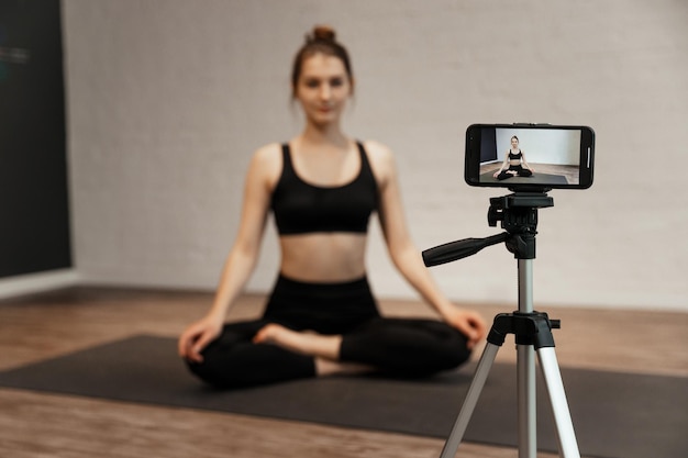 Jeune blogueuse femme avec caméra sur trépied enregistrant un studio de yoga en ligne