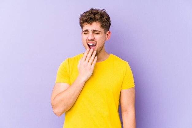 Jeune blond cheveux bouclés homme bâillant montrant un geste fatigué couvrant la bouche avec la main