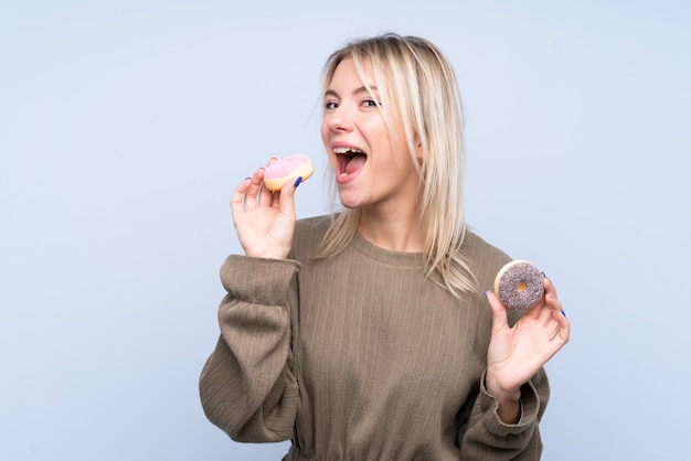 Jeune, blond, femme, isolé, bleu, mur, manger, beignet