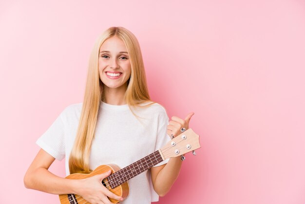 Jeune, blond, femme, jouer, ukelele, sourire, élévation, pouce, haut