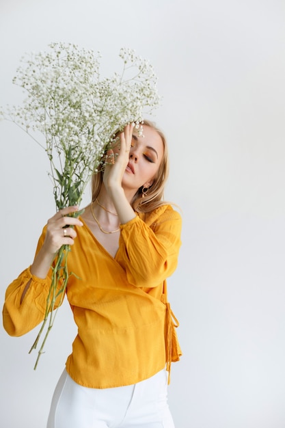 Une jeune blonde aux fleurs sèches se couvre le visage de sa main. maquillage à la mode