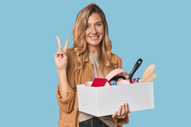 Jeune blonde blanche se déplaçant avec une boîte joyeuse et insouciante montrant un symbole de paix avec des doigts