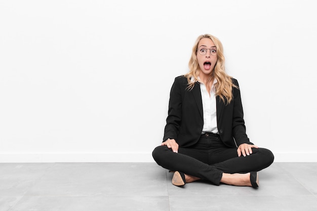 Jeune blonde businesswoman sitting on a cement floor sentiment choqué