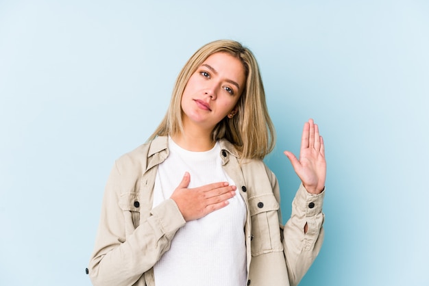 Jeune blonde caucasienne femme isolée prêtant serment, mettant la main sur la poitrine.