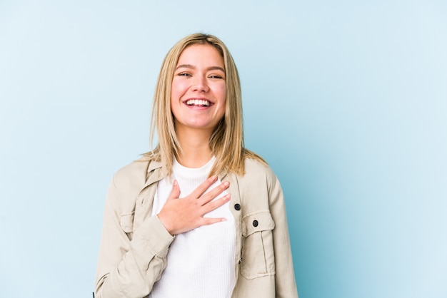 Jeune blonde caucasienne femme isolée rit à haute voix en gardant la main sur la poitrine.