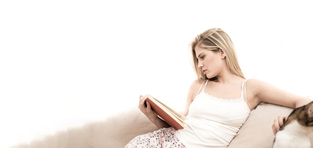 Photo une jeune blonde est assise sur un canapé et lit un livre pendant qu'elle lit le livre elle caresse son chat elle est très sérieuse