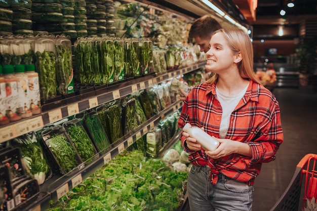 Jeune blonde femme joyeuse en épicerie en choisissant des verts