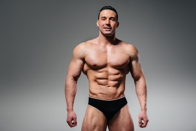 Un jeune bodybuilder athlète pose dans le studio seins nus, montrant ses abdominaux et ses muscles