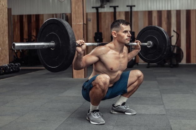 Jeune bodybuilder masculin musclé faisant des squats avec une barre sur ses épaules dans un club de santé moderne. Musculation et Fitness