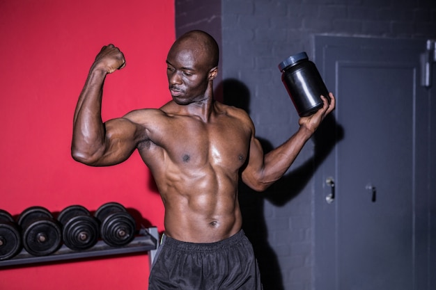 Jeune bodybuilder regardant ses muscles tout en tenant une bouteille