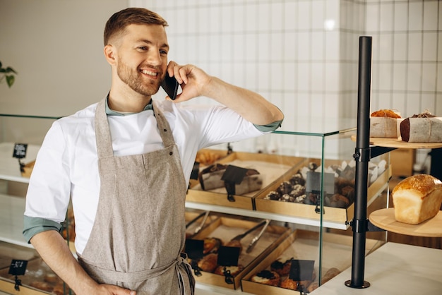 Jeune boulanger debout près du comptoir et parler au téléphone