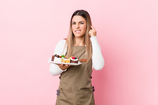 Jeune boulanger femme tenant des bonbons couvrant les oreilles avec les mains