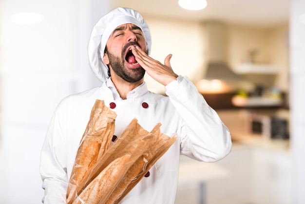 Le jeune boulanger prend du pain et bâille dans la cuisine