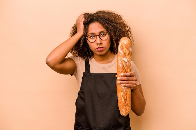 Jeune boulangère femme africaine tenant une miche de pain isolée sur fond beige étant choquée, elle s'est souvenue d'une réunion importante