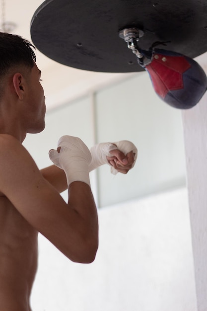 Jeune boxeur latin frappant à l'entraînement le sac de boxe avec ses poings bandés