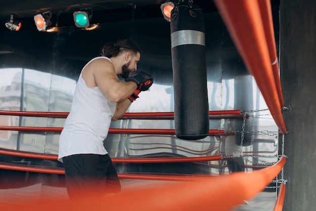 Jeune boxeur professionnel sur le ring, pratique la technique des frappes, du rack, de la défense et de l'endurance, mouillé à l'entraînement, devant la caméra