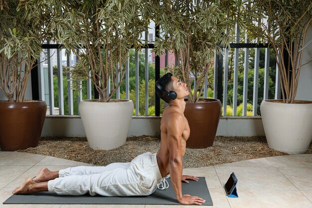 Jeune Brésilien prenant des cours de yoga en ligne avec casque, en position de yoga chien orienté vers le haut.