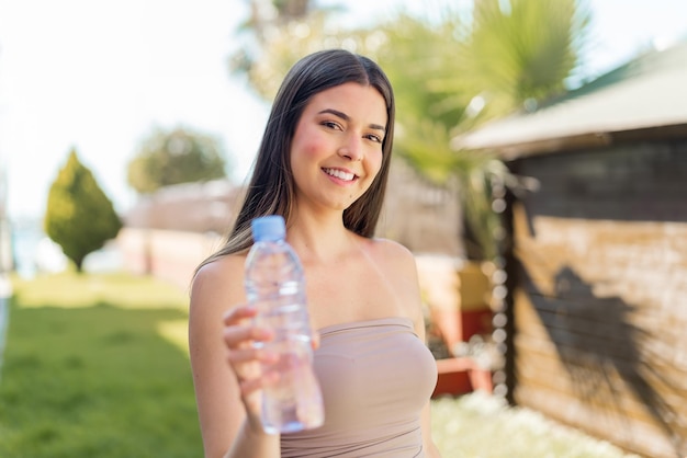 Une jeune Brésilienne avec une bouteille d'eau à l'extérieur avec une expression heureuse