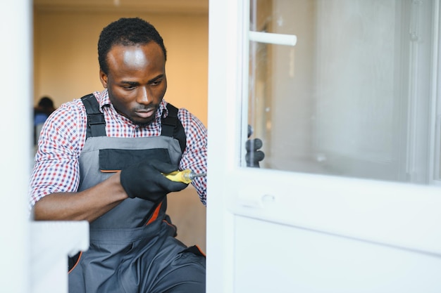 Jeune bricoleur africain en uniforme réparant une fenêtre de verre avec un tournevis