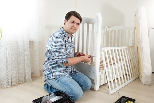 Jeune bricoleur assis sur le sol dans une pièce vide et assemblant de nouveaux meubles