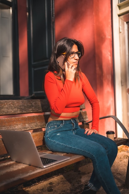 Jeune brune assise sur un banc dans le parc avec ordinateur portable