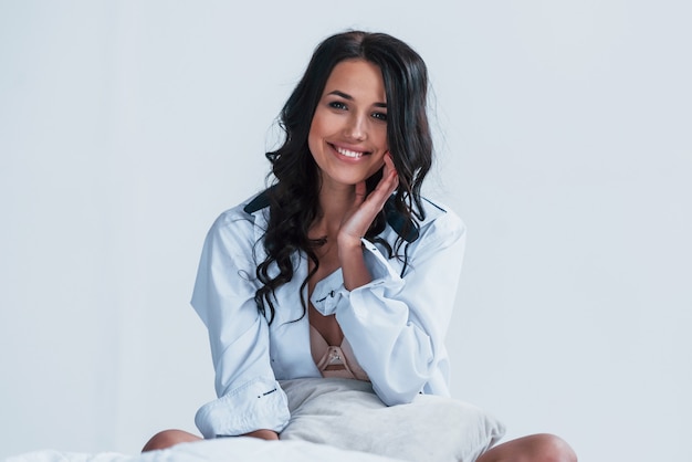 Jeune brune en blouse blanche assise sur le lit dans la salle blanche.