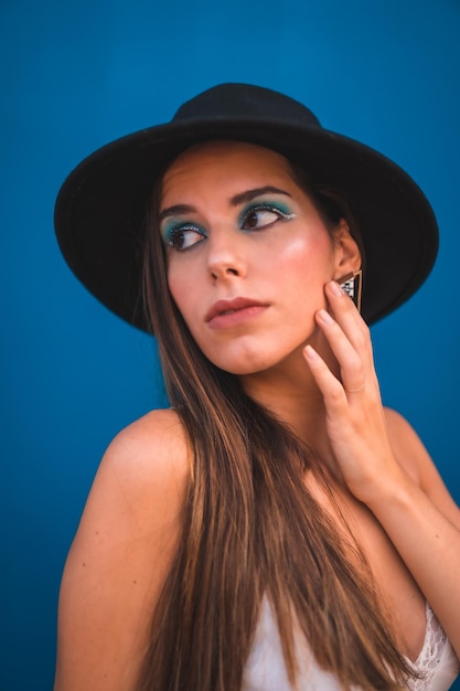 Une jeune brune dans un chapeau noir et un t-shirt blanc sur fond bleu