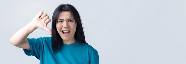 Jeune brune dans un débardeur bleu donnant le geste du pouce vers le bas regardant avec une expression négative