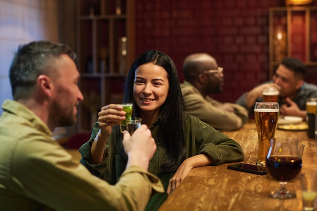 Une jeune brune heureuse avec un verre d'apéritif en train de faire un toast avec son petit ami.