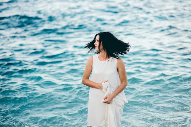 Jeune brune sexy dans l&#39;eau bleue vêtue d&#39;une robe blanche sur la plage en Grèce