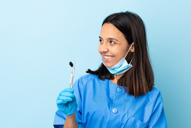 Jeune brunette métisse dentiste femme tenant des outils sur isolé heureux et souriant