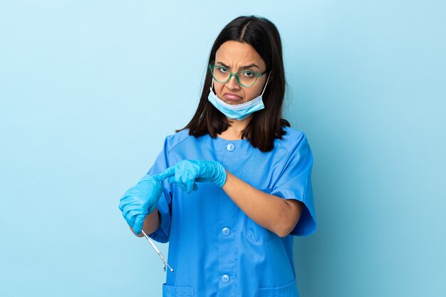 Jeune brunette métisse dentiste femme tenant des outils sur un mur isolé faisant le geste d'être en retard