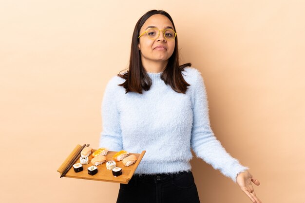 Jeune brunette race mixte woman holding sushi sur mur isolé ayant des doutes