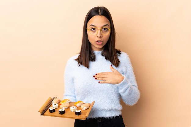 Jeune brunette race mixte woman holding sushi sur mur surpris et choqué tout en regardant à droite