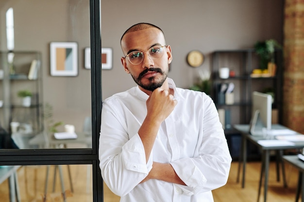 Jeune bureau de directeur général masculin confiant debout contre l'intérieur du bureau