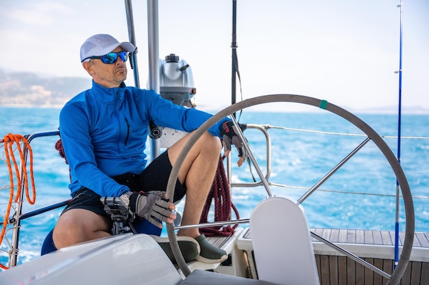 Le jeune capitaine se tient à la barre et contrôle un voilier lors d'un voyage en mer