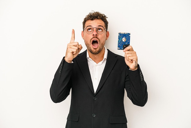 Jeune caucasien informatisé tenant le disque dur isolé sur fond blanc pointant vers le haut avec la bouche ouverte.