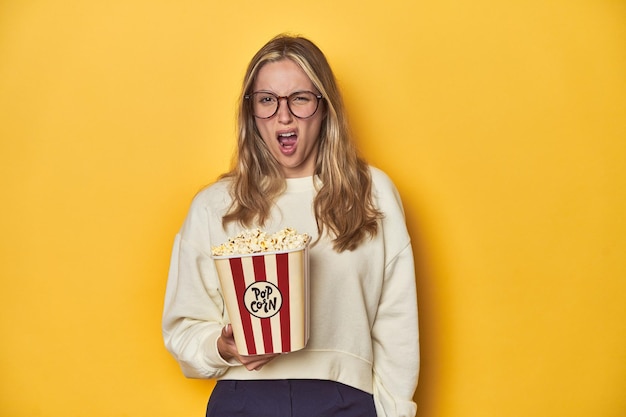 Jeune Caucasien tenant un concept de cinéma de pop-corn sur fond jaune criant très en colère et agressif