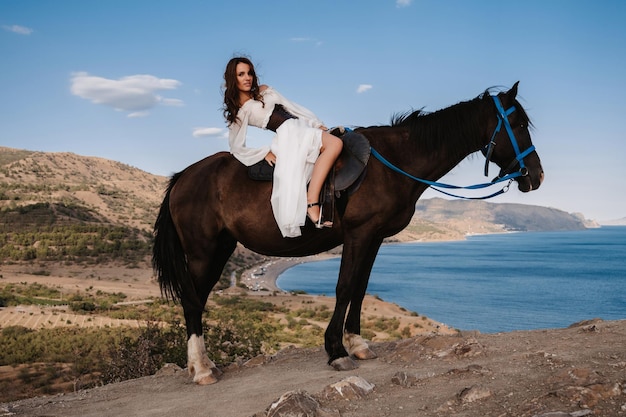 Une jeune cavalière vêtue d'une robe blanche pose en selle sur un cheval appuyé contre un magnifique paysage de montagne Le concept de contes de fées romantiques Exemple d'une couverture de livre finie