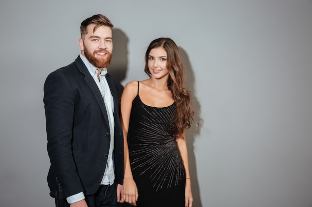 Jeune ccouple souriant en vêtements intelligents debout et regardant à l'avant sur un mur gris