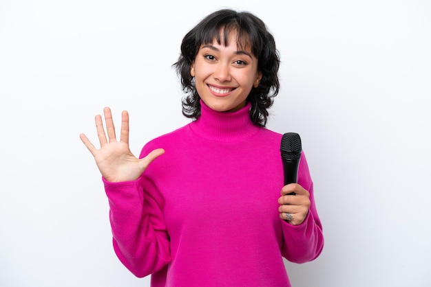 Une jeune chanteuse argentine isolée sur un fond blanc compte cinq avec ses doigts.