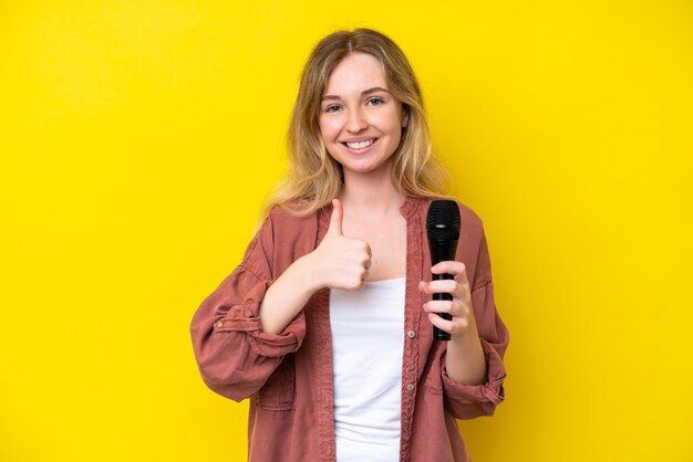 Jeune chanteuse caucasienne prenant un microphone isolé sur fond jaune donnant un geste du pouce levé