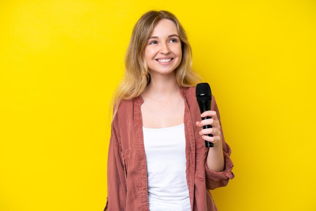 Jeune chanteuse caucasienne prenant un microphone isolé sur fond jaune en pensant à une idée tout en levant les yeux