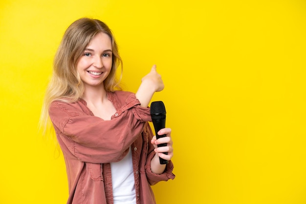 Jeune chanteuse caucasienne prenant un microphone isolé sur fond jaune pointant vers l'arrière