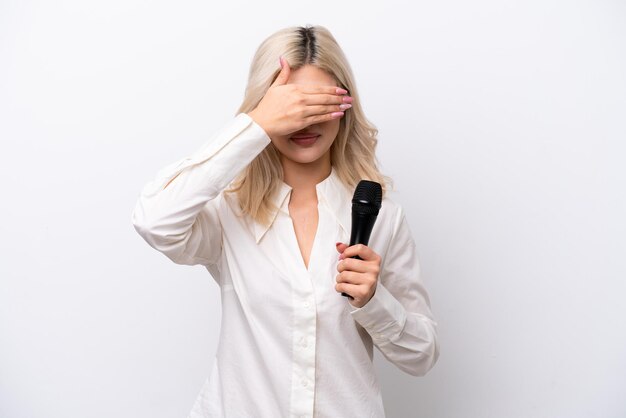 Jeune chanteuse femme prenant un microphone isolé sur fond blanc couvrant les yeux par les mains Je ne veux pas voir quelque chose