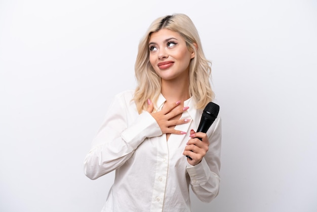 Jeune chanteuse femme prenant un microphone isolé sur fond blanc en levant tout en souriant